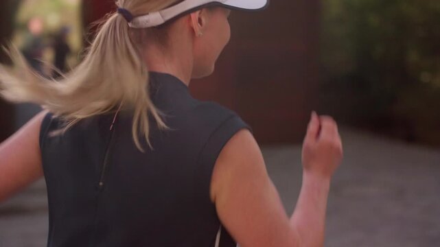 Woman runs through a forest trail. She wears a cap and athletic gear. Her focused expression shows determination and energy. This footage suits fitness, wellness, or outdoor adventure themes