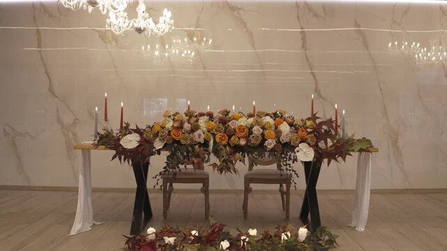 Wedding sweetheart table with autumn roses and candles under chandelier against marble wall