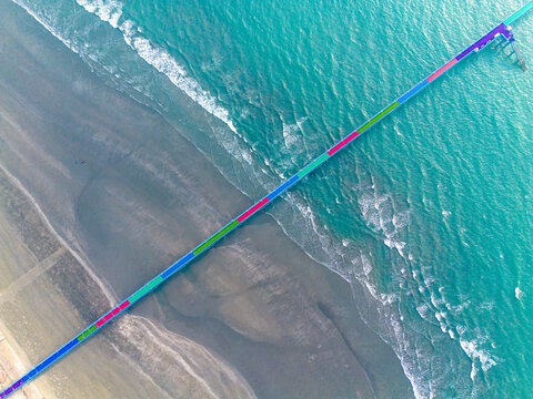 Aerial view of a vibrant pier stretching into the turquoise sea, contrasting with the textured sandy beach below, Cox's Bazar, Chittagong Division, Bangladesh.