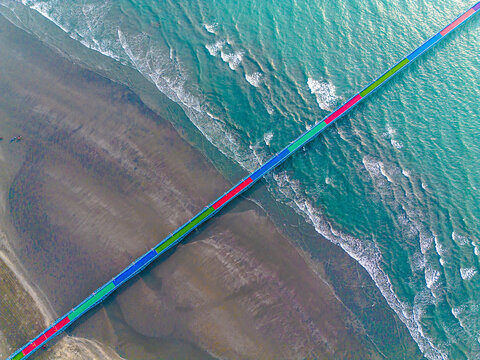 Aerial view of a vibrant, long bridge stretching across the meeting point of sandy shores and turquoise waves, Cox's Bazar, Chittagong Division, Bangladesh.