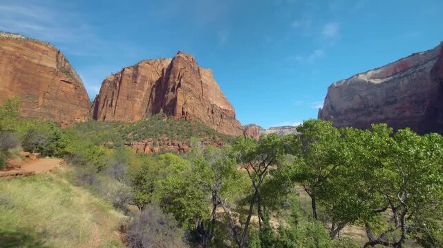 Footage capturing the stunning natural beauty of the Emerald Pools Trail in Zion National Park, Utah, USA. The scene features lush green trees and vegetation contrasting with towering red sandstone cl