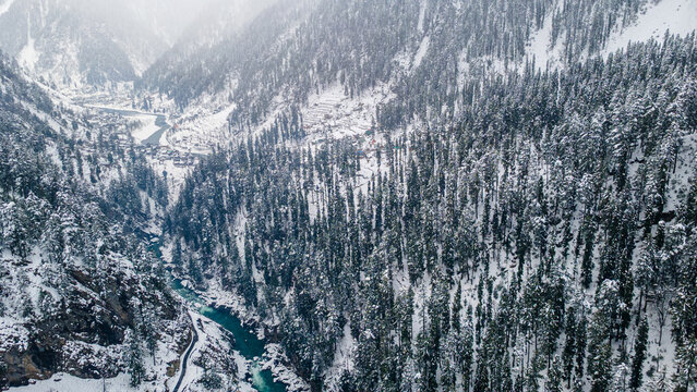 Aerial view of the dazzling contrast of the turquoise river cutting through the snow-laden forest, Sharda, Azad Kashmir, Pakistan.
