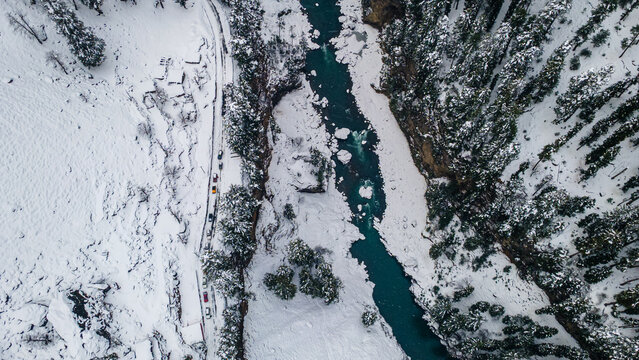 Aerial view of the turquoise river cutting through the snow-laden landscape, framed by dense, dark coniferous trees, Sharda, Azad Kashmir, Pakistan.