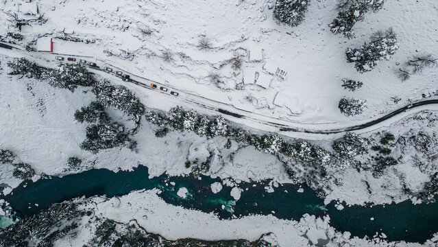 Aerial view of a serpentine road cuts through a snow-laden landscape, where the turquoise river contrasts with the stark white, Sharda, Azad Kashmir, Pakistan.