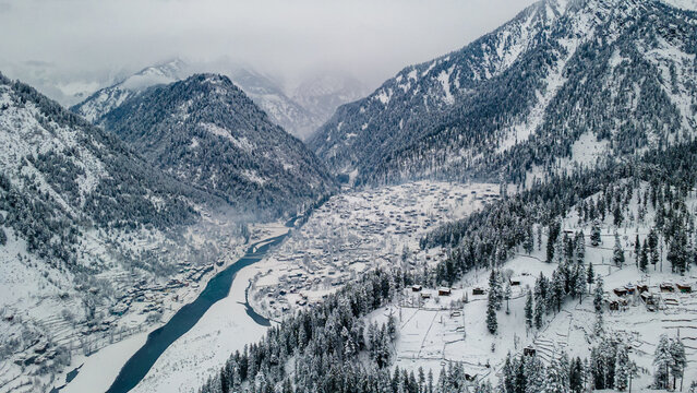 Aerial view of a snow-laden Sharda nestled in a valley, the river snaking through the landscape, framed by majestic mountains, Sharda, Azad Kashmir, Pakistan.