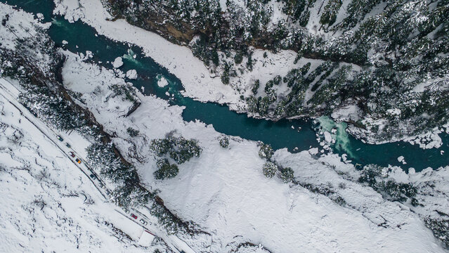 Aerial view of a turquoise river winding through a snow-laden valley, contrasting with the dark evergreens clinging to the steep slopes, Sharda, Azad Kashmir, Pakistan.
