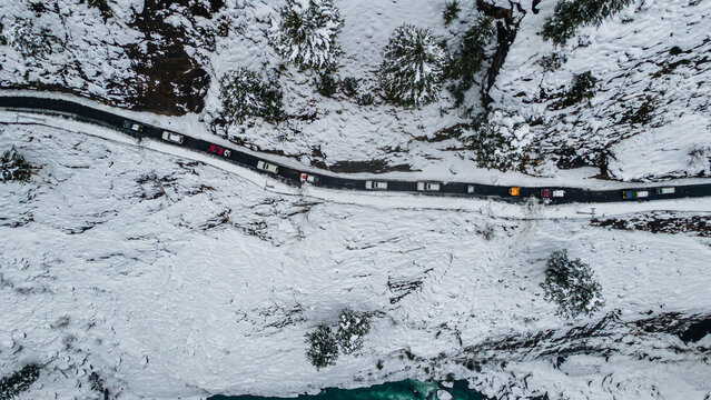 Aerial view of a winding road snaking through a snow-laden valley, where a line of cars navigates the wintry landscape, Sharda, Azad Kashmir, Pakistan.