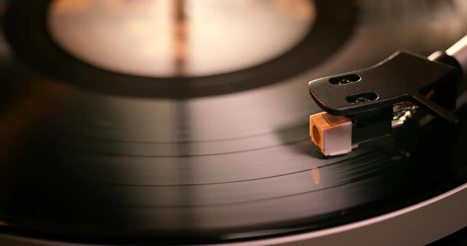 Detailed close-up of a turntable tonearm with white cartridge headshell, positioned over a black vinyl record on the platter, highlighting audio equipment precision.