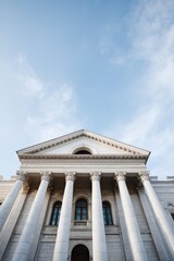Fototapeta premium Grand neoclassical courthouse facade with towering corinthian columns, triangular pediment and arched entrance under soft sky, monumental white stone architecture in low angle view