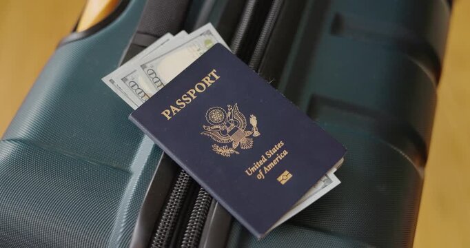  Hand placing United States passport with dollar bills inside on travel luggage preparing for trip