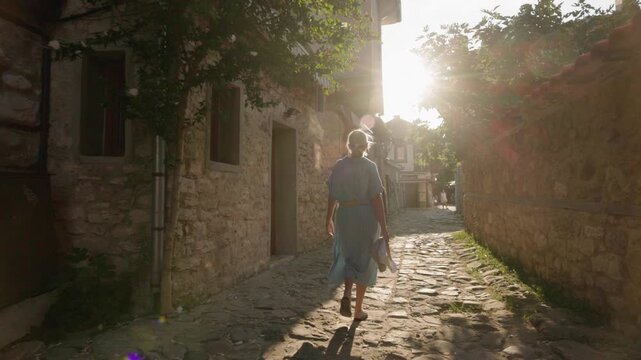 Woman walking along cobblestone street in old Nessebar with sunlight and flare