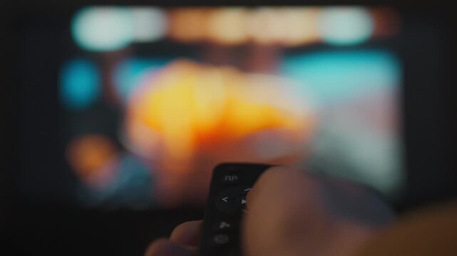 A young man spends the evening comfortably on the sofa in a home theater. With the remote control in his hands, he switches TV channels, enjoying his favorite programs and films