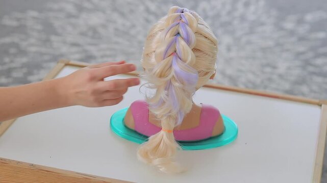 Hand touching dragon braid on child mannequin head with blonde hair