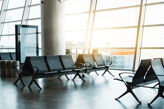 Empty airport terminal with waiting seats and bright sun shining through large windows