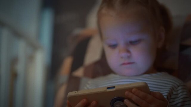 A young child sits comfortably on a sofa, engrossed in vibrant cartoons on a smartphone screen during a serene evening, prompting parental concern about potential eyesight risks under lax supervision