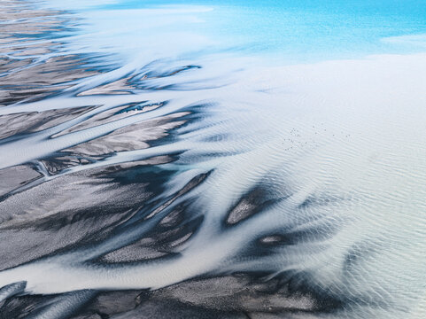 Aerial view of braided rivers create a stark contrast against the turquoise waters, as nature's artistry unfolds from above, Lake Tekapo, Canterbury Region, New Zealand.