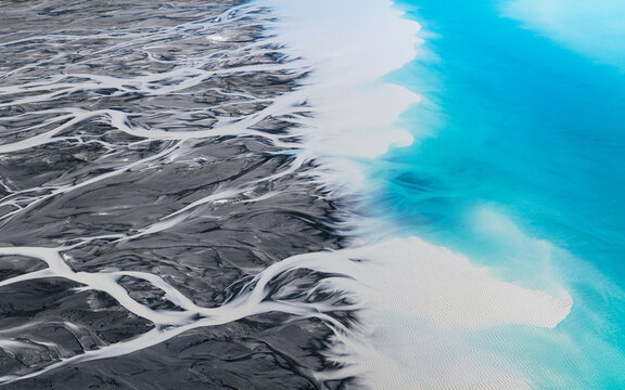 Aerial view of the braided river contrasting sharply with the turquoise waters of Lake Tekapo, Lake Tekapo, Canterbury Region, New Zealand.
