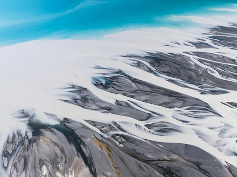 Aerial view of glacial rivers carving paths through the landscape, turquoise waters meeting stony banks, a symphony of nature's artistry, Lake Tekapo, Canterbury Region, New Zealand.