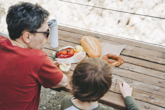Close-up view of father and his school boy son on a family picnic in the mountains. Child kid and his dad taking a rest and enjoying a picnic while hiking in the mountains.