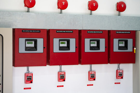 Row of industrial fire control panels with manual alarm stations and bell devices mounted on a wall, representing emergency response systems, safety monitoring, and facility protection.