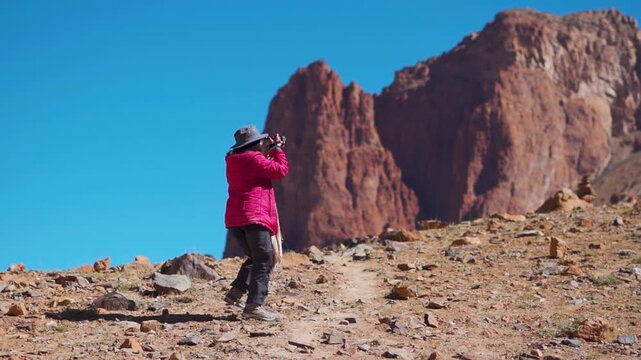 Young Indian female traveler taking photo or video with her camera in front of rocky Himalayan mountain in the remote region of Zanskar valley in Ladakh, India. Girl taking photo for her social media.