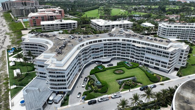 Aerial view of luxurious condos meet the ocean's edge, with manicured lawns and a golf course in the distance, Palm Beach, Florida, United States.