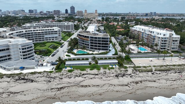 Aerial view of pristine white buildings lining the beach, contrasting with the deep blue pools and the distant city skyline, Palm Beach, Florida, United States.