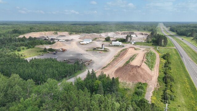 Aerial view of a quarry site contrasting starkly against the surrounding lush greenery and a distant highway, Grand Rapids, Minnesota, United States.