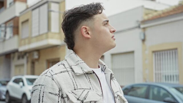 Man looking up, profile and bare neck visible on a residential street with parked cars and building facades; quiet contemplation.