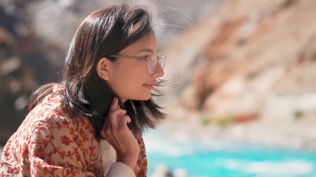 Portrait of teenager Indian girl sitting near flowing Tsarap river in Zanskar, Ladakh, India. Indian woman portrait in nature. Adventure travel concept. Hiker girl relaxing in mountains after trek. 