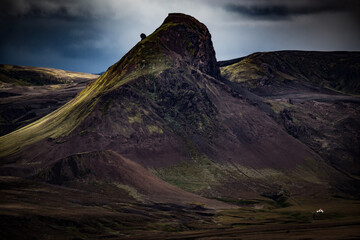 A towering volcanic mountain looms over a small house in Iceland