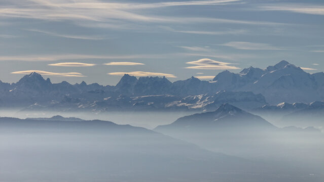 Aerial view of the majestic, snow-capped mountains piercing through a sea of ethereal fog, casting long shadows across the undulating landscape, Gex, Auvergne-Rhone-Alpes, France.