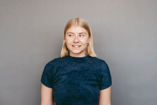 Smiling young woman with blond hair giving sideways glance against gray background