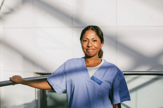 Portrait of smiling female medical professional standing near railing in hospital corridor