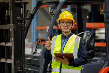 An adult Asian male, a warehouse technician, wearing a safety helmet and vest, checks inventory in an industrial plant.