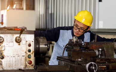 An Asian man, an industrial machinist, is operating a lathe in a factory to perform mechanical maintenance and manufacture high-precision parts.
