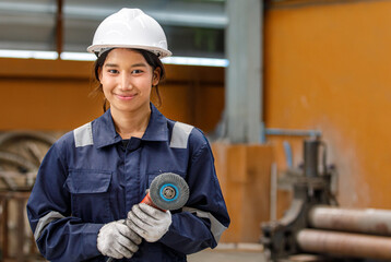 The image of an Asian female worker wearing a safety helmet and holding a grinder in a factory conveys her confidence as a technician.