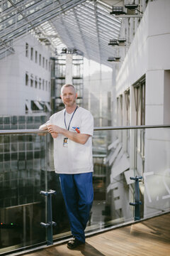 Full length portrait of male healthcare worker standing near railing in hospital corridor