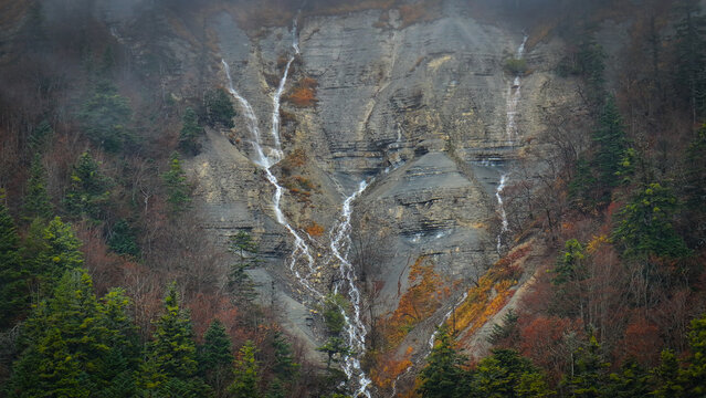 Aerial view of cascading waters gracefully descend the rugged rock face, embraced by autumn-tinged foliage, painting a serene yet dramatic scene, Gex, Auvergne-Rhone-Alpes, France.