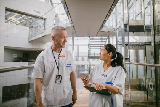 Female medical expert holding file folder discussing with male coworker while standing in hospital corridor