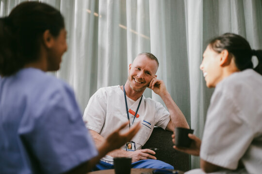 Smiling male medical worker spending leisure time with female coworkers at coffee break in hospital lobby