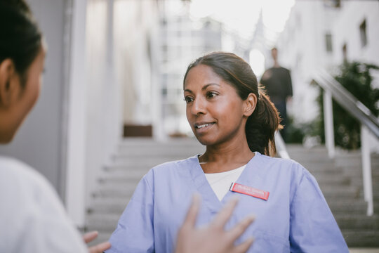 Female medical expert listening to colleague consoling her while standing in hospital lobby