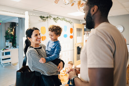 Happy woman talking with male teacher while holding son during first day of school