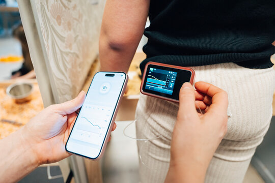 Female teacher examining glucose level of girl through insulin pump and smart phone app
