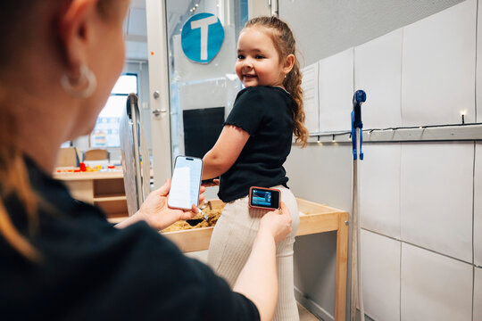 Smiling girl looking at teacher measuring glucose level through smart phone app and insulin pump