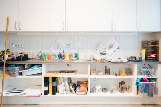 Organized craft storage area in classroom with white cabinets and open shelves