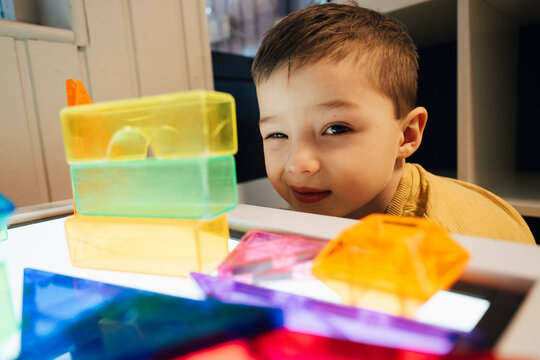Portrait of cute boy winking while playing with colorful geometric shapes at table in classroom