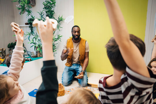 Mature male teacher doing activity with children holding alphabets in preschool classroom