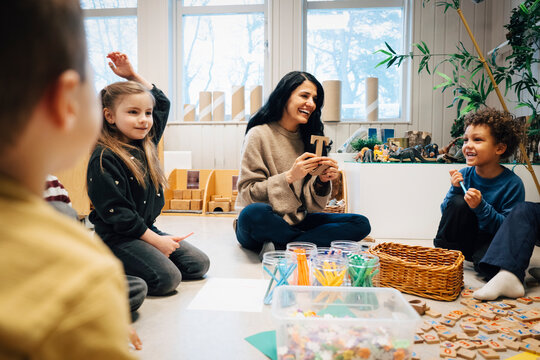 Happy female teacher doing fun and interactive session with children sitting on classroom floor