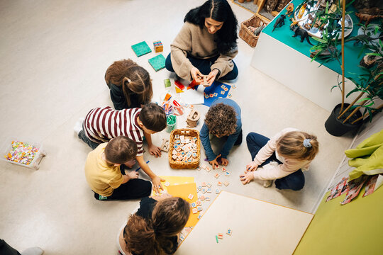 High angle view of female teacher sitting with elementary children doing fun activity in classroom at preschool